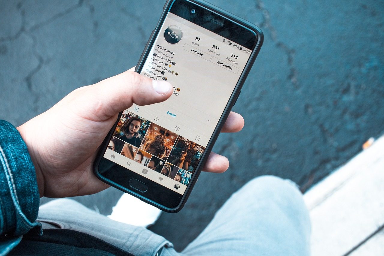 Main tenant un téléphone affichant un profil de réseau social avec son compteur d'abonnés