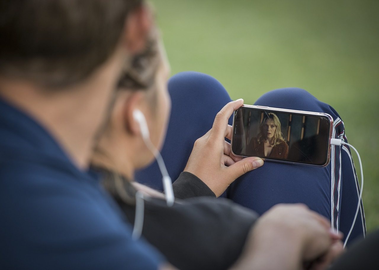 Deux personnes partageant des écouteurs pour regarder une vidéo sur un téléphone